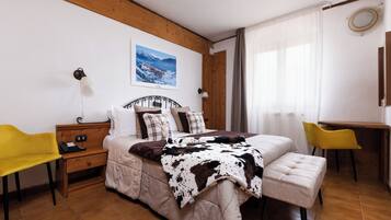 A bedroom with a bed, bedside tables, a desk, chairs, and a painting on the wall.