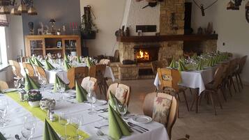 A dining area with tables set for a meal, a stone fireplace, and a wooden cabinet with decorative items.