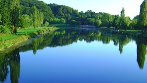 A calm lake with reflections of trees and a distant building, surrounded by lush greenery. - Landgasthof Ralinger Hof (Ralingen)