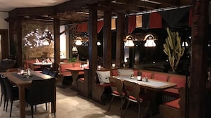 A restaurant with wooden tables and booths, stone walls, and hanging pendant lights. - Landgasthof Ralinger Hof (Ralingen)
