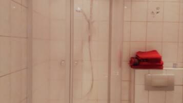 A bathroom with a tiled wall, a shower area, and a towel rack with a red towel.