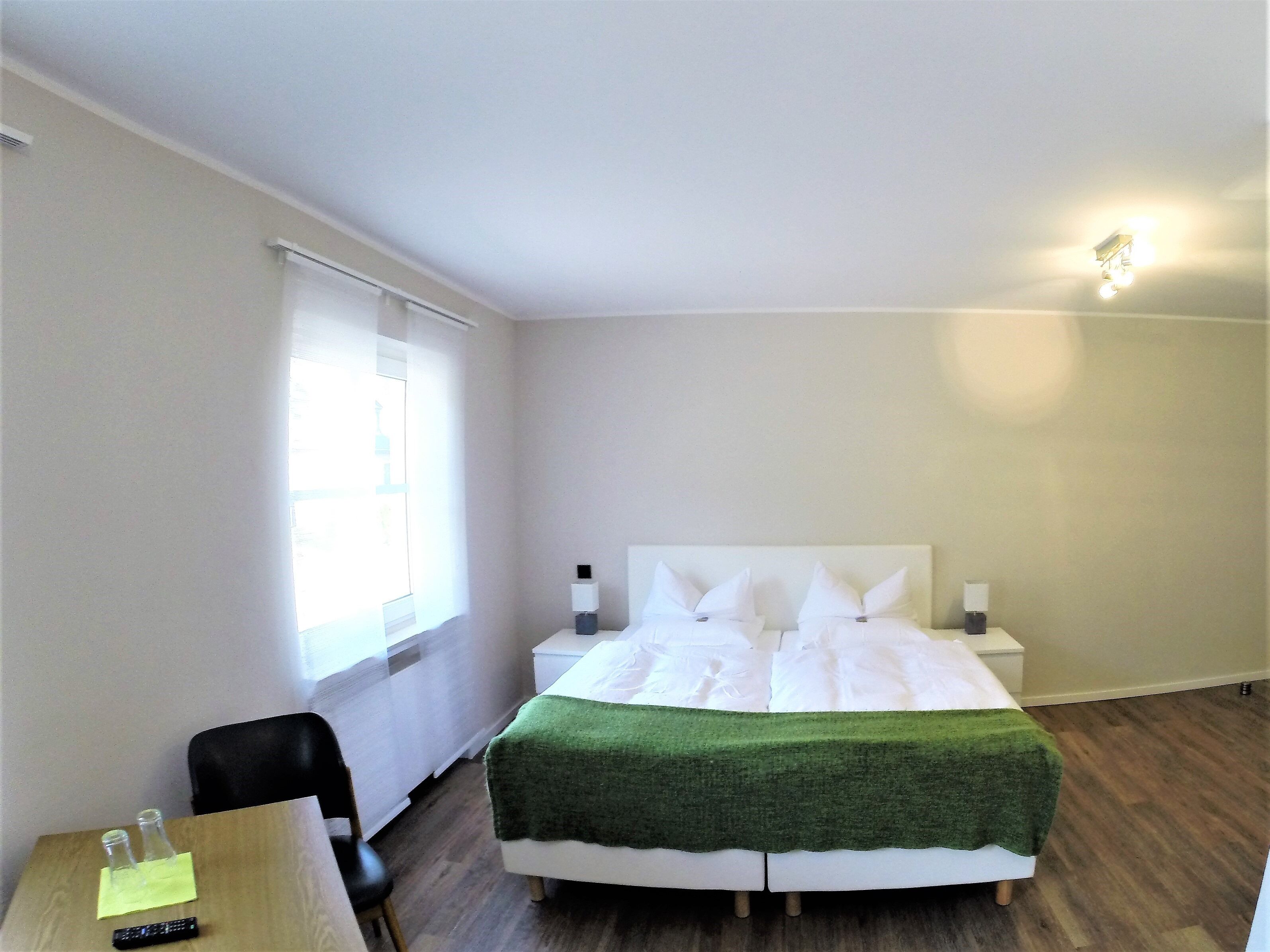 A hotel room with a double bed, bedside tables, a desk with a chair, and a window with blinds.
