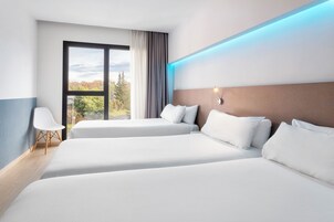 Habitación de hotel con dos camas, un ventanal con vistas a árboles y una lámpara moderna.
