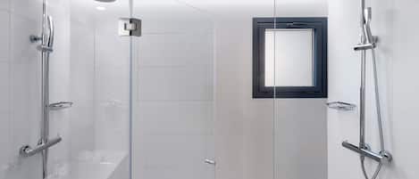 Un área de ducha moderna con puertas de vidrio, un cabezal de ducha de mano, un cabezal de ducha empotrado y un ventanal.