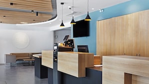 Een moderne hotel receptie met een houten balie, een flatscreen televisie en een zithoek met een bank en stoelen.