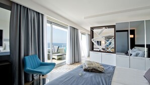 A modern hotel room with a bed, a blue chair, a desk, and a large window offering a view of the sea. - Selene Beach & Spa Hotel (Alanya)