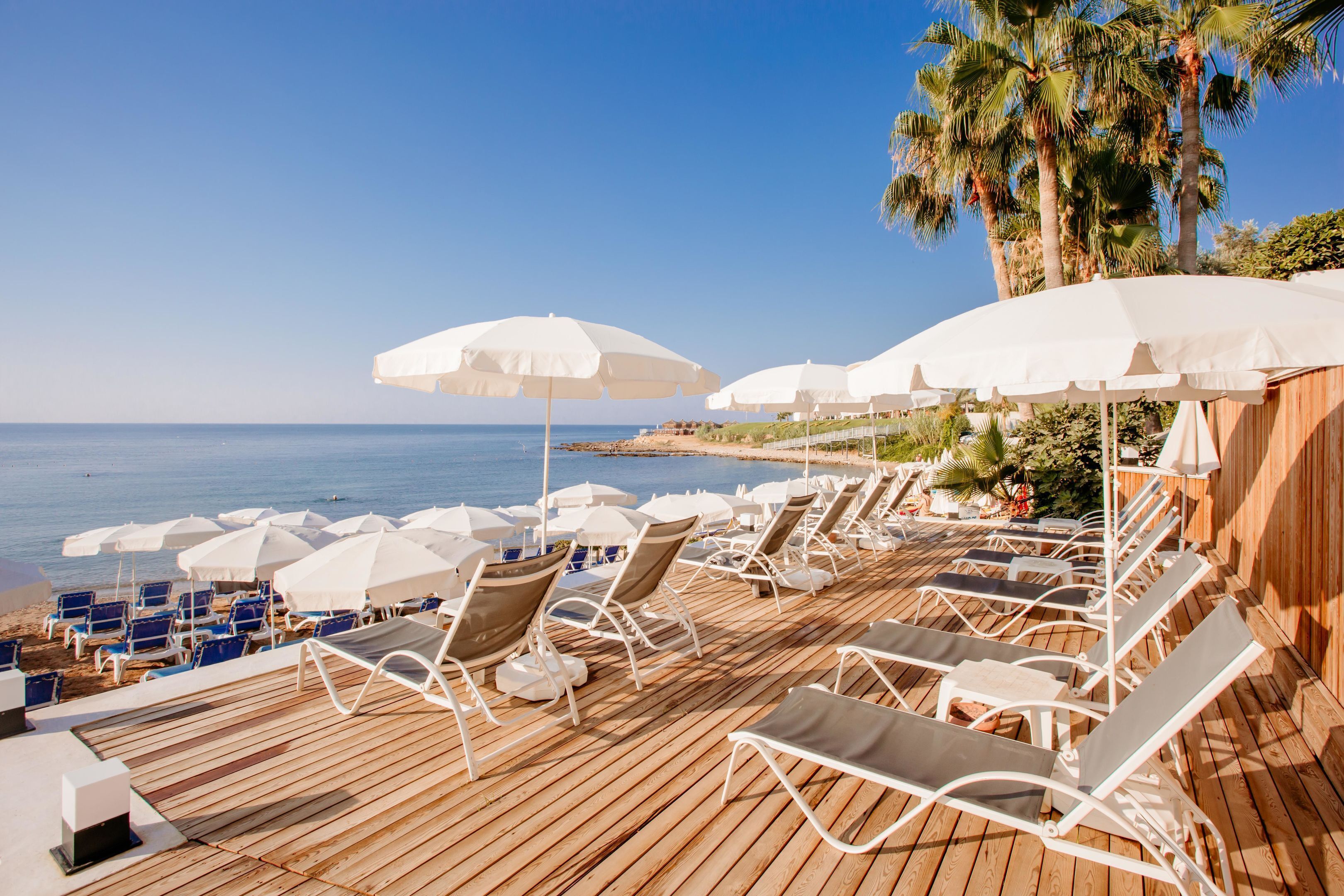 A wooden deck with white sun umbrellas and lounge chairs facing a beach.