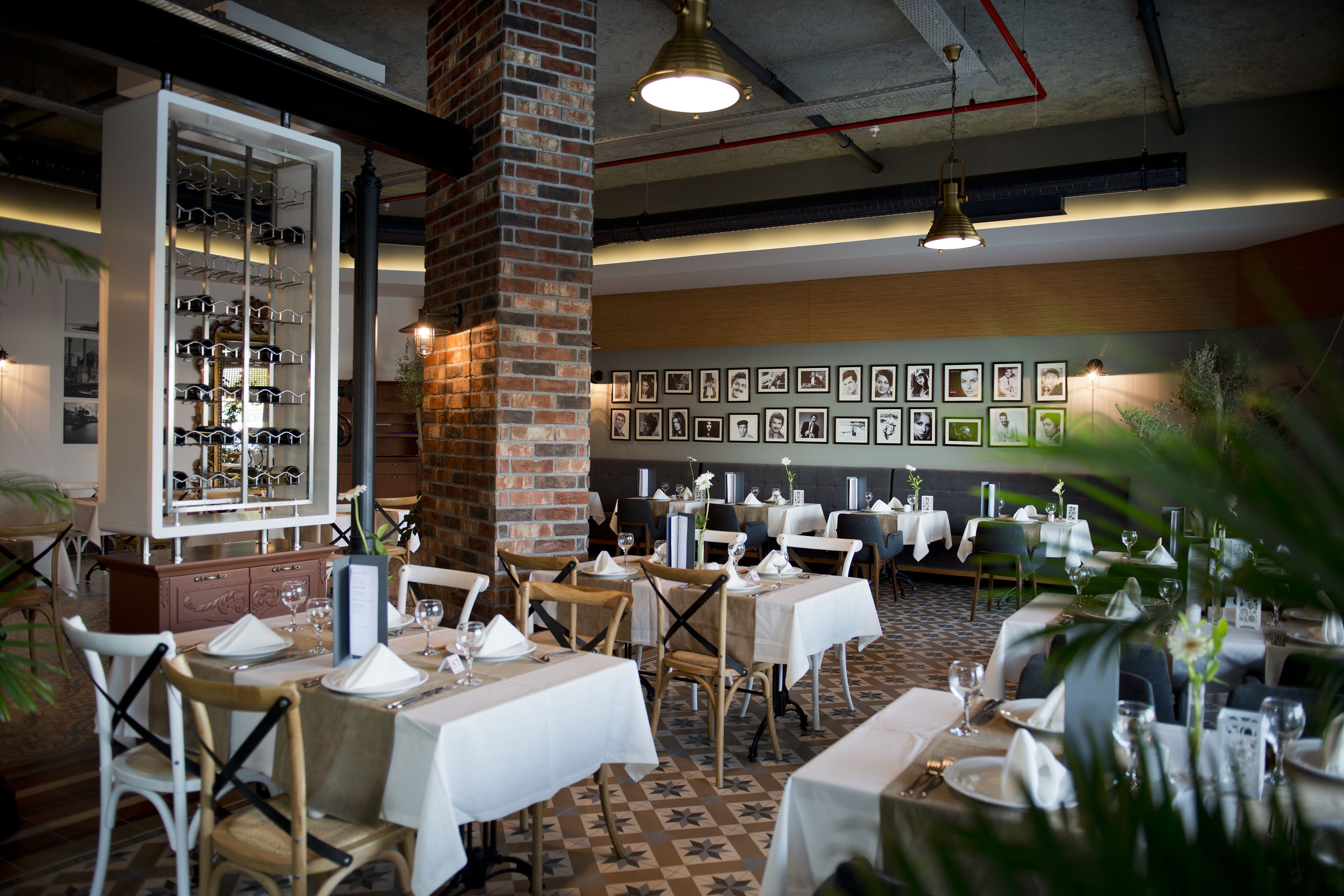 Um restaurante com mesas montadas para refeições, um espaço para vinhos e quadros nas paredes.