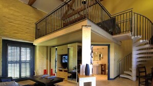 A spacious living area with a high ceiling, a staircase leading to an upper floor, and a large window with blinds. - Corran Resort & Spa (Carmarthen)