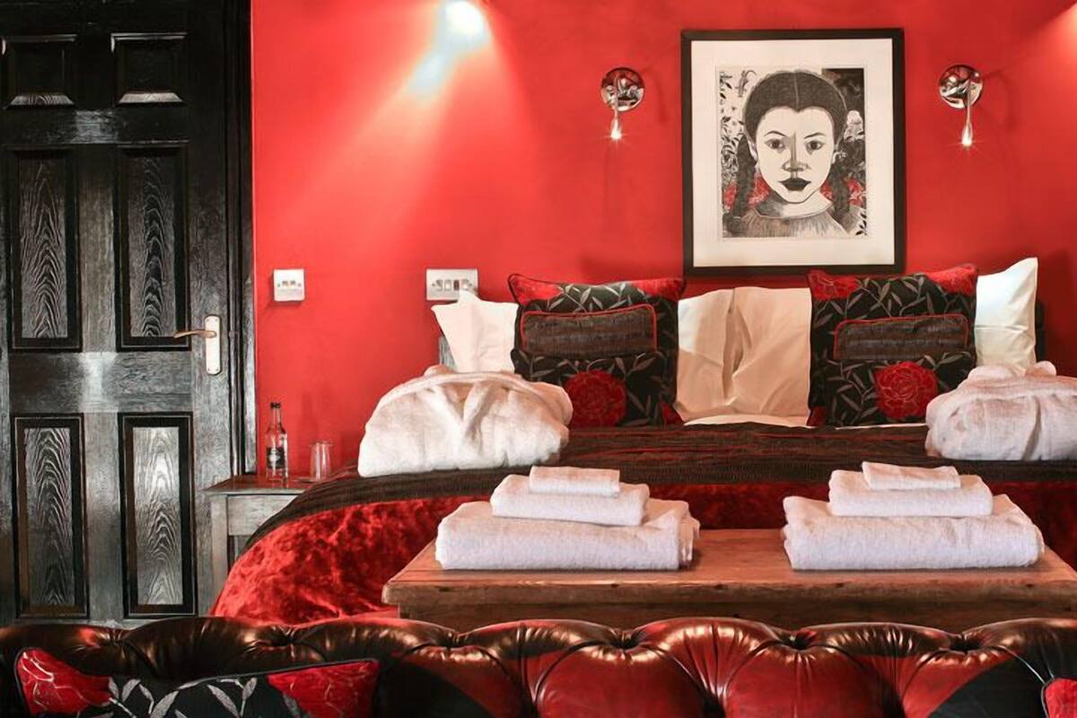 Quarto com decoração em vermelho, uma cama grande, duas mesas laterais, um espelho e uma obra de arte emoldurada na parede.