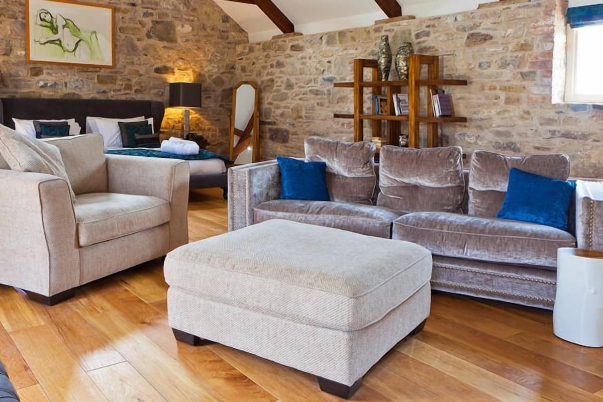 Uma sala de estar aconchegante com parede de pedra, um sofá, uma mesa de centro e uma área de jantar com mesa e cadeiras.