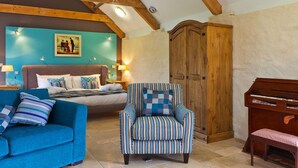 A cozy room with a bed, a blue sofa, a striped armchair, a wooden piano, and a large wooden wardrobe. - Corran Resort & Spa (Carmarthen)