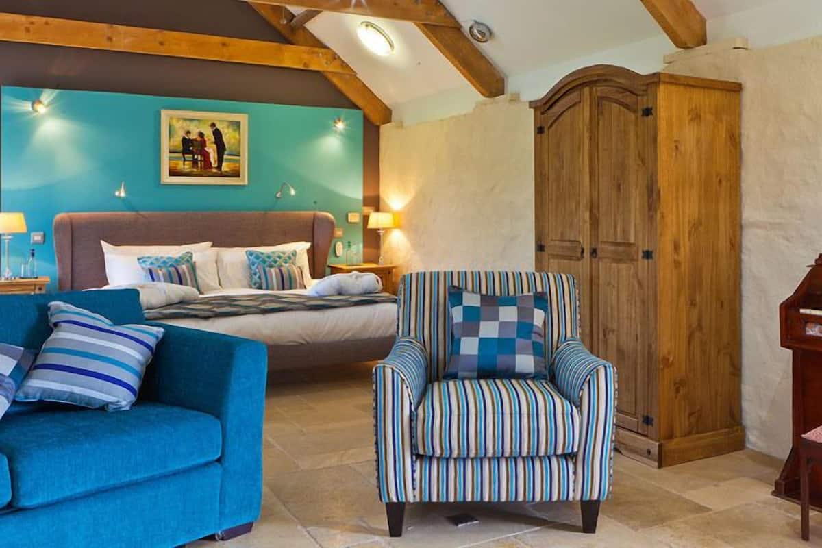 Quarto aconchegante com uma cama, um sofá azul, uma poltrona listrada, um piano de madeira e um guarda-roupa grande de madeira.