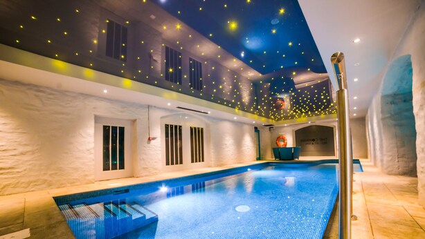 An indoor swimming pool with a blue tiled floor, a diving board, and a ceiling decorated with star-like lights. - Corran Resort & Spa (Carmarthen)