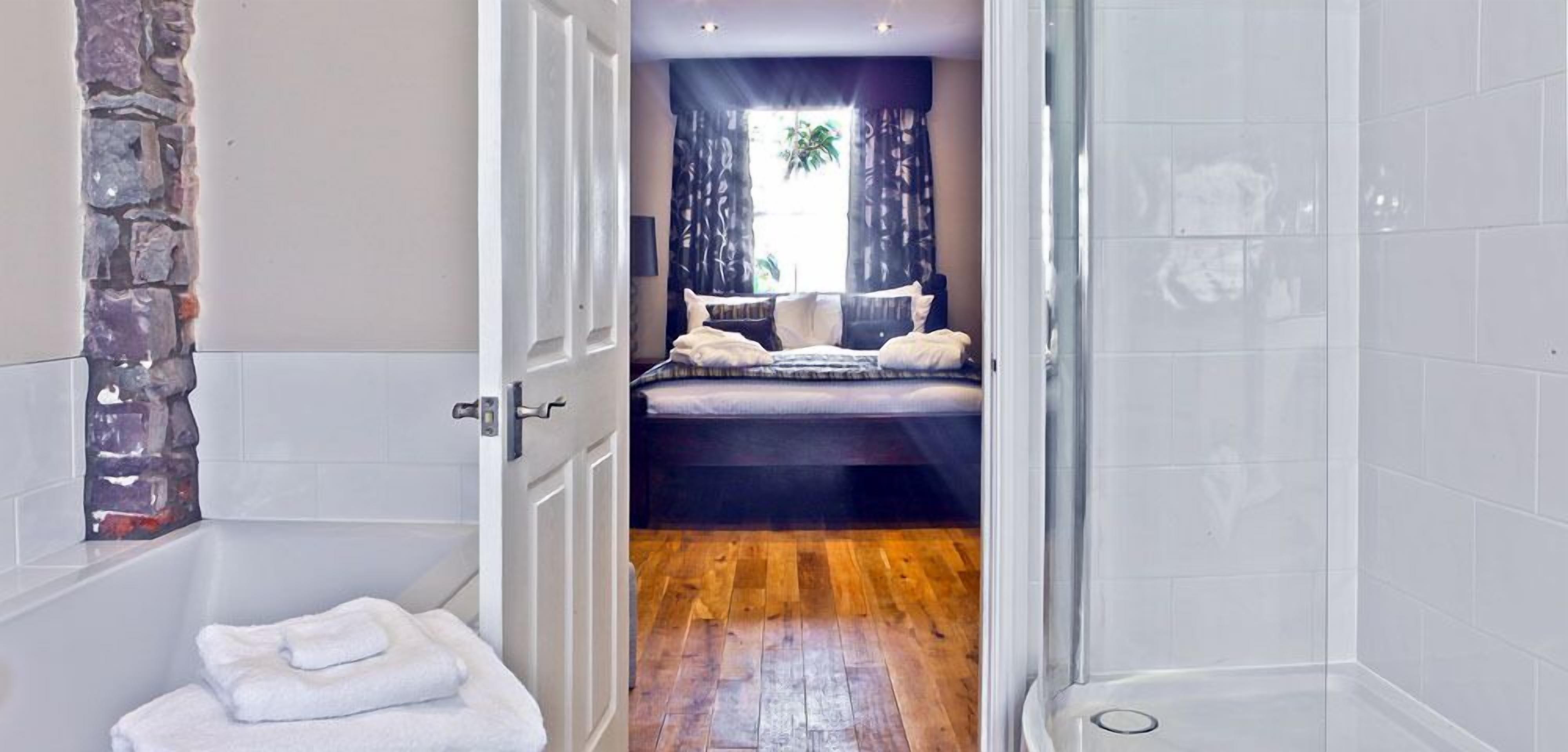 A bathroom with a stone accent wall, a bathtub, and a wooden floor.