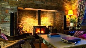 A cozy room with a stone wall, a fireplace, a sofa, a table with books, and a lamp. - Corran Resort & Spa (Carmarthen)