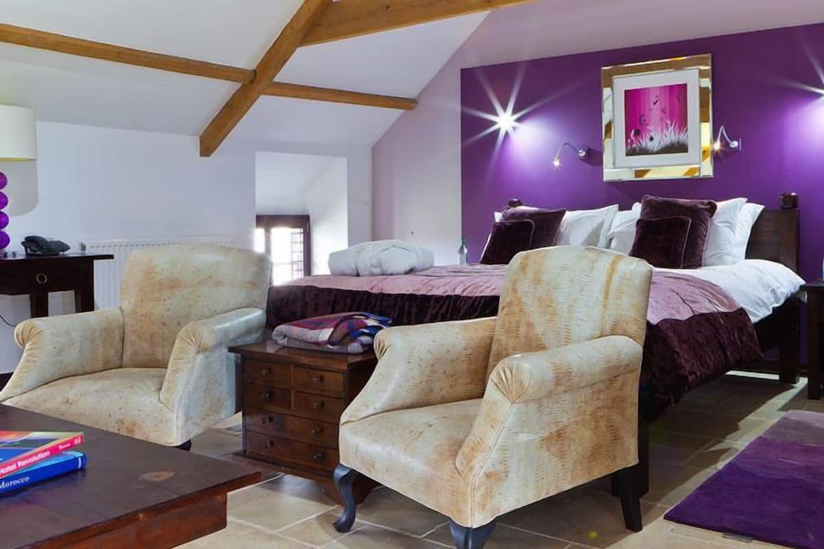 Um quarto com uma cama, duas poltronas, uma mesinha de cabeceira e um guarda-roupa.
