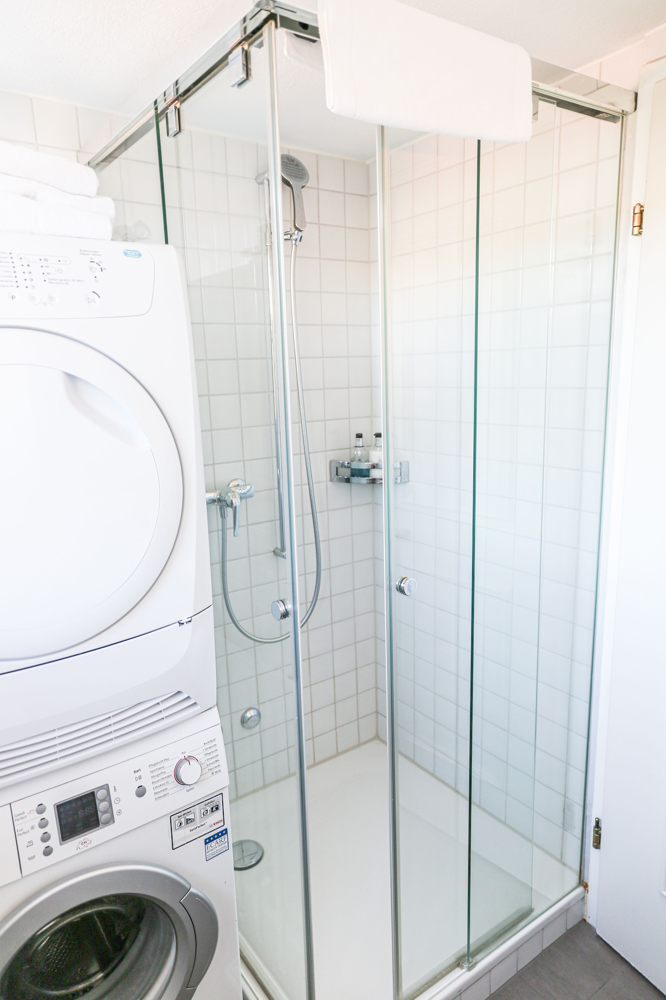 Ein modernes Badezimmer mit einer gläsernen Duschkabine, einer integrierten Waschmaschine und gefliesten Wänden.