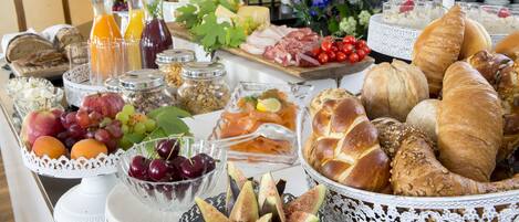 A buffet table with various food items including fruits, cheeses, meats, and breads.