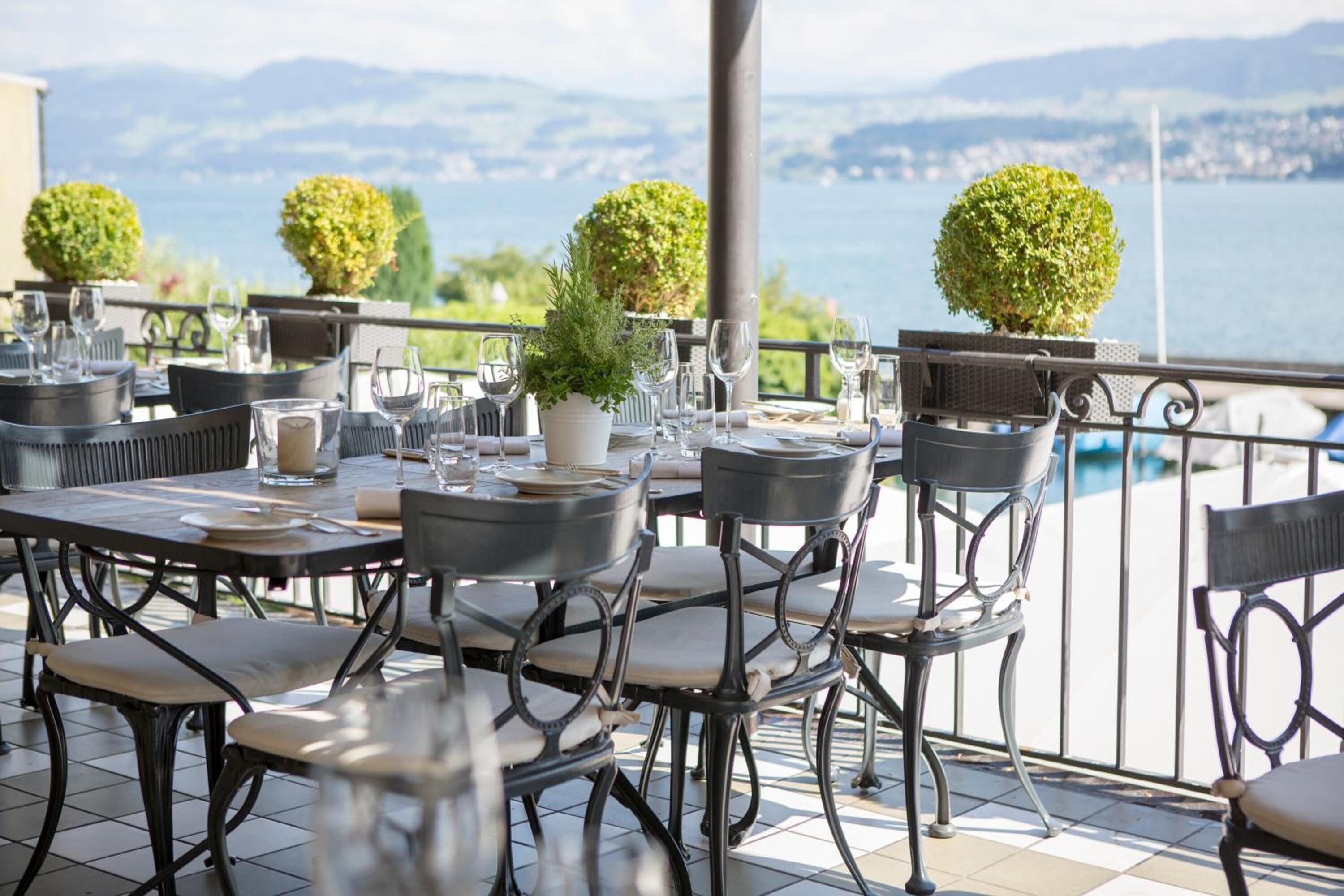 Una terraza con mesas dispuestas para comer, plantas en macetas y vistas al mar.