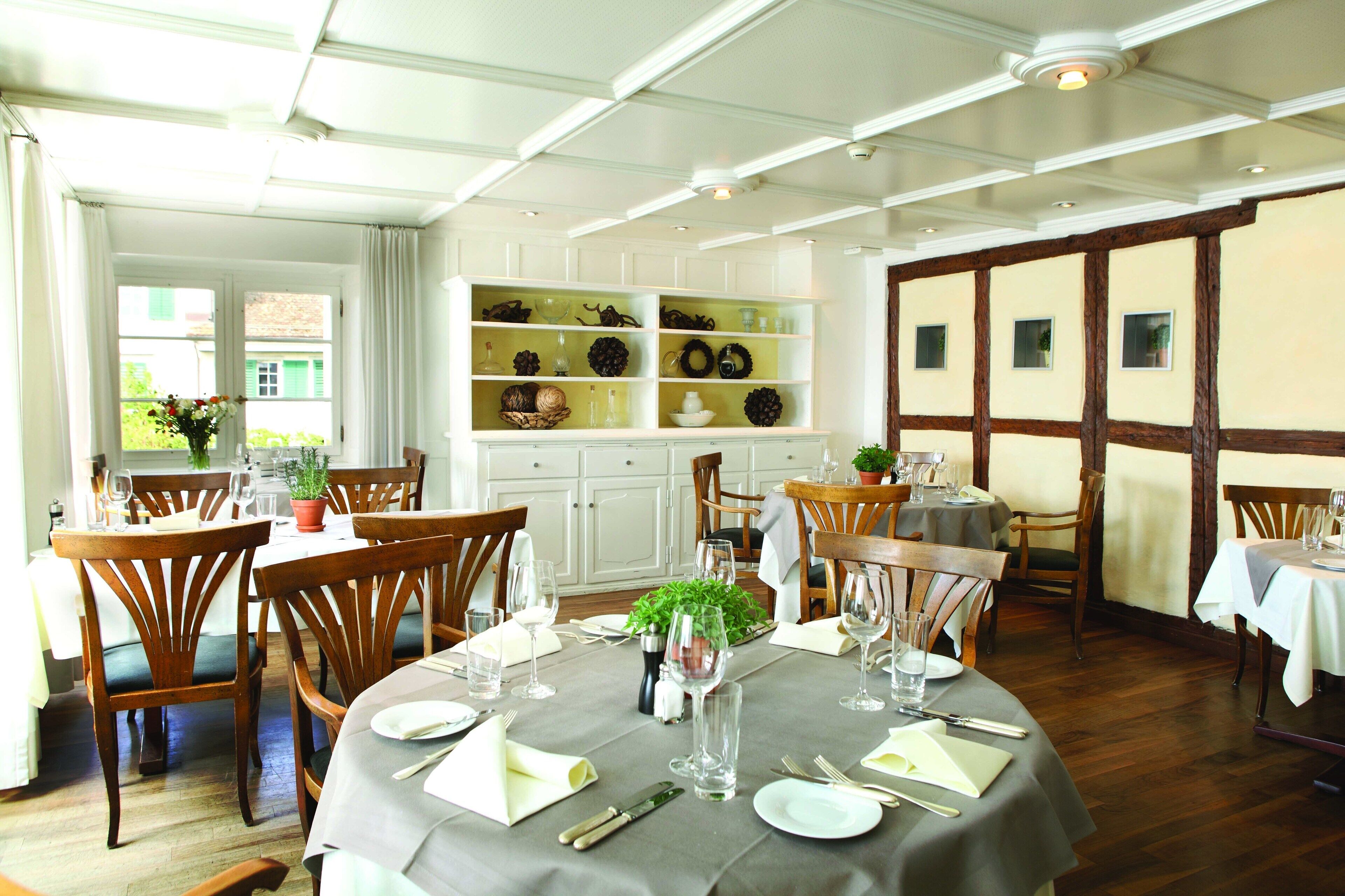 A dining area with wooden chairs, round tables, and a white ceiling with exposed beams.
