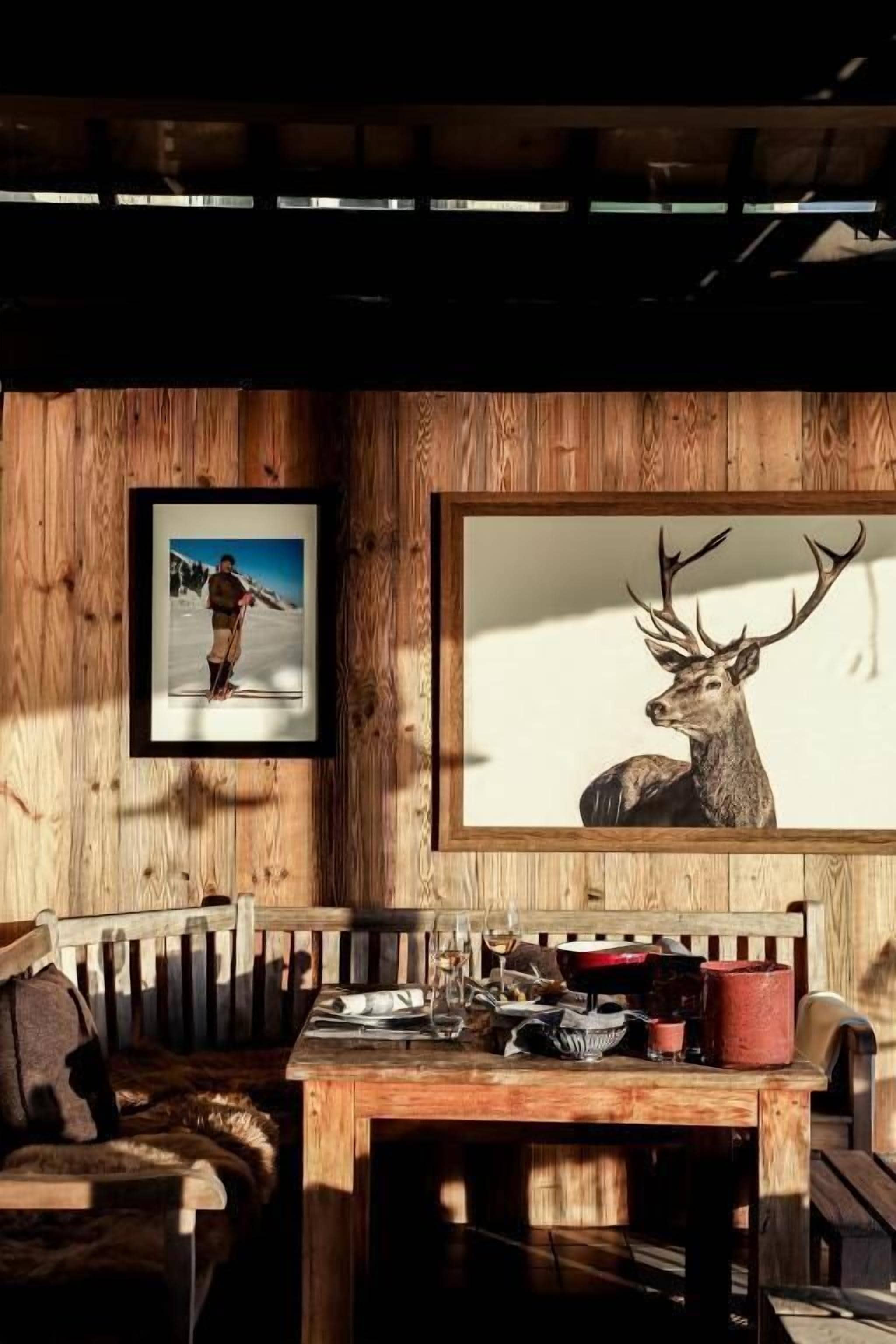 Un intérieur en bois avec un banc en bois, une table sur laquelle se trouvent divers objets, et deux tableaux encadrés accrochés au mur.