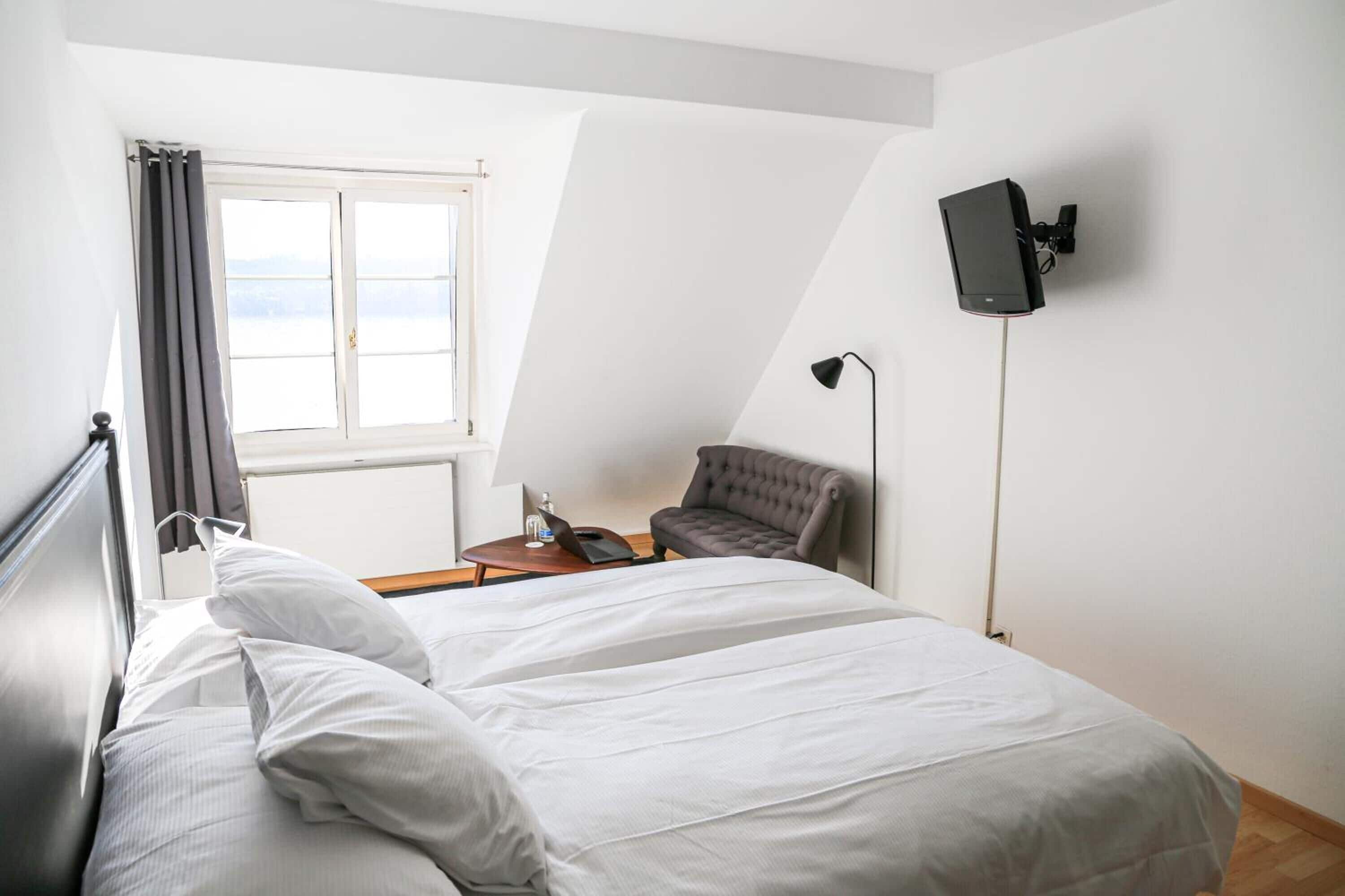Een slaapkamer met een bed, een stoel, een bureau, een lamp en een tv aan de muur.