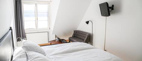 Een slaapkamer met een bed, een stoel, een bureau, een lamp en een tv aan de muur.