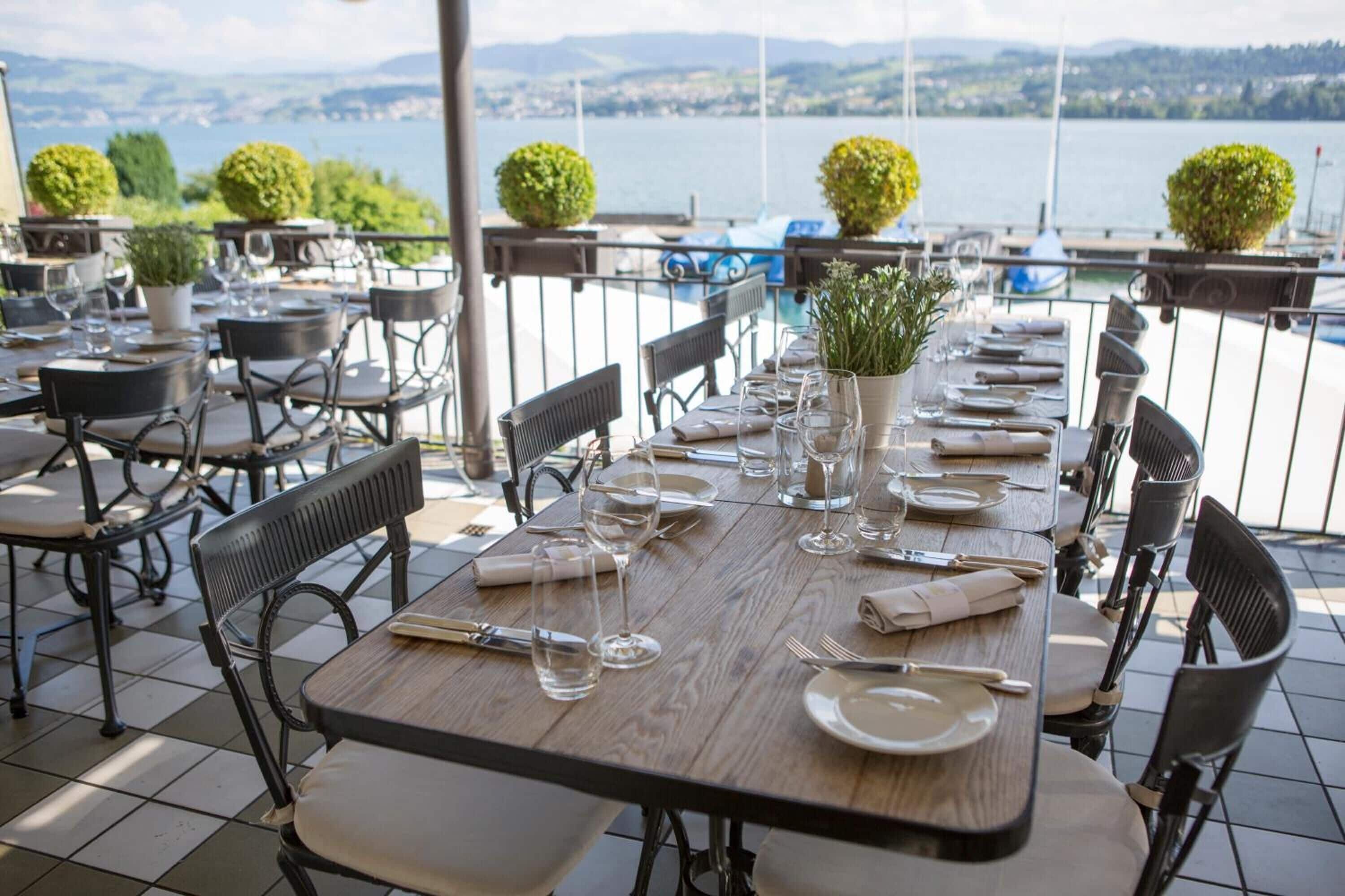 Mesa de comedor dispuesta para seis personas, con sillas, un jarrón con plantas y vistas al lago y las montañas.
