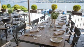 Mesa de comedor dispuesta para seis personas, con sillas, un jarrón con plantas y vistas al lago y las montañas.