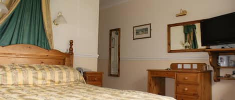 A bedroom with a bed, a wooden dresser, a desk, a mirror, and a television.