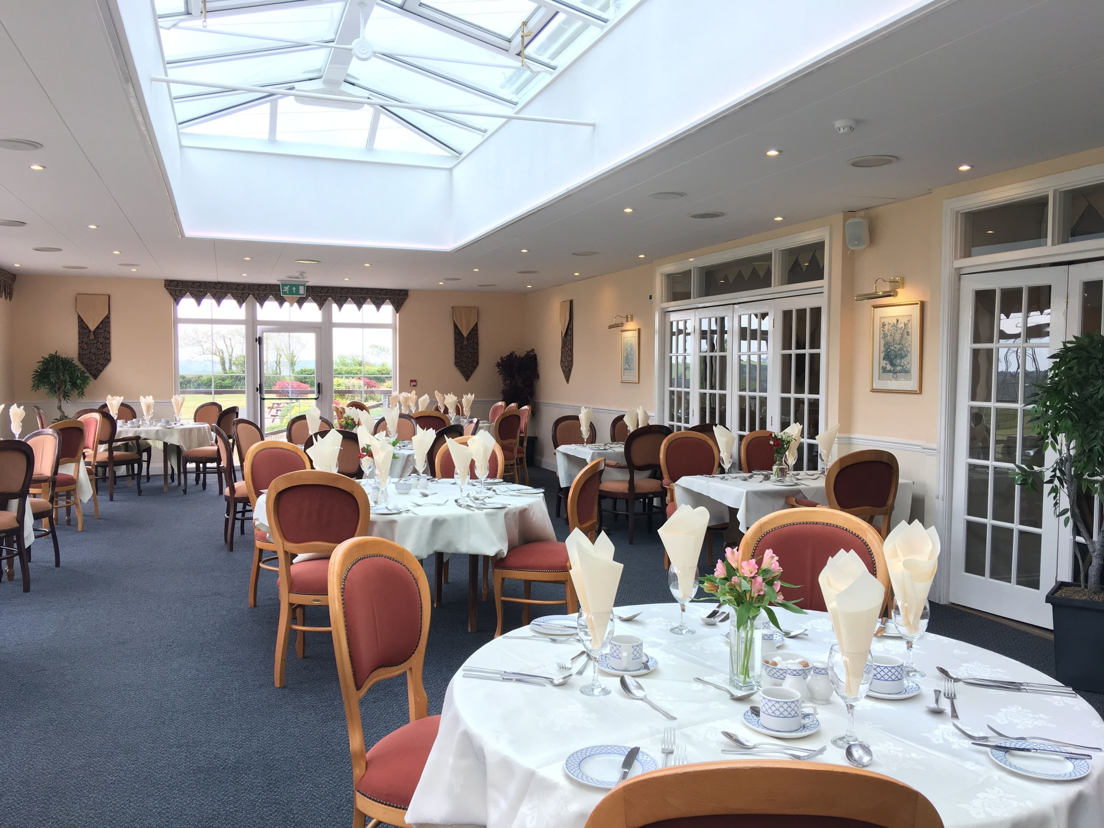 Een restaurant met ronde tafels, stoelen en een hoge plafond met dakramen.