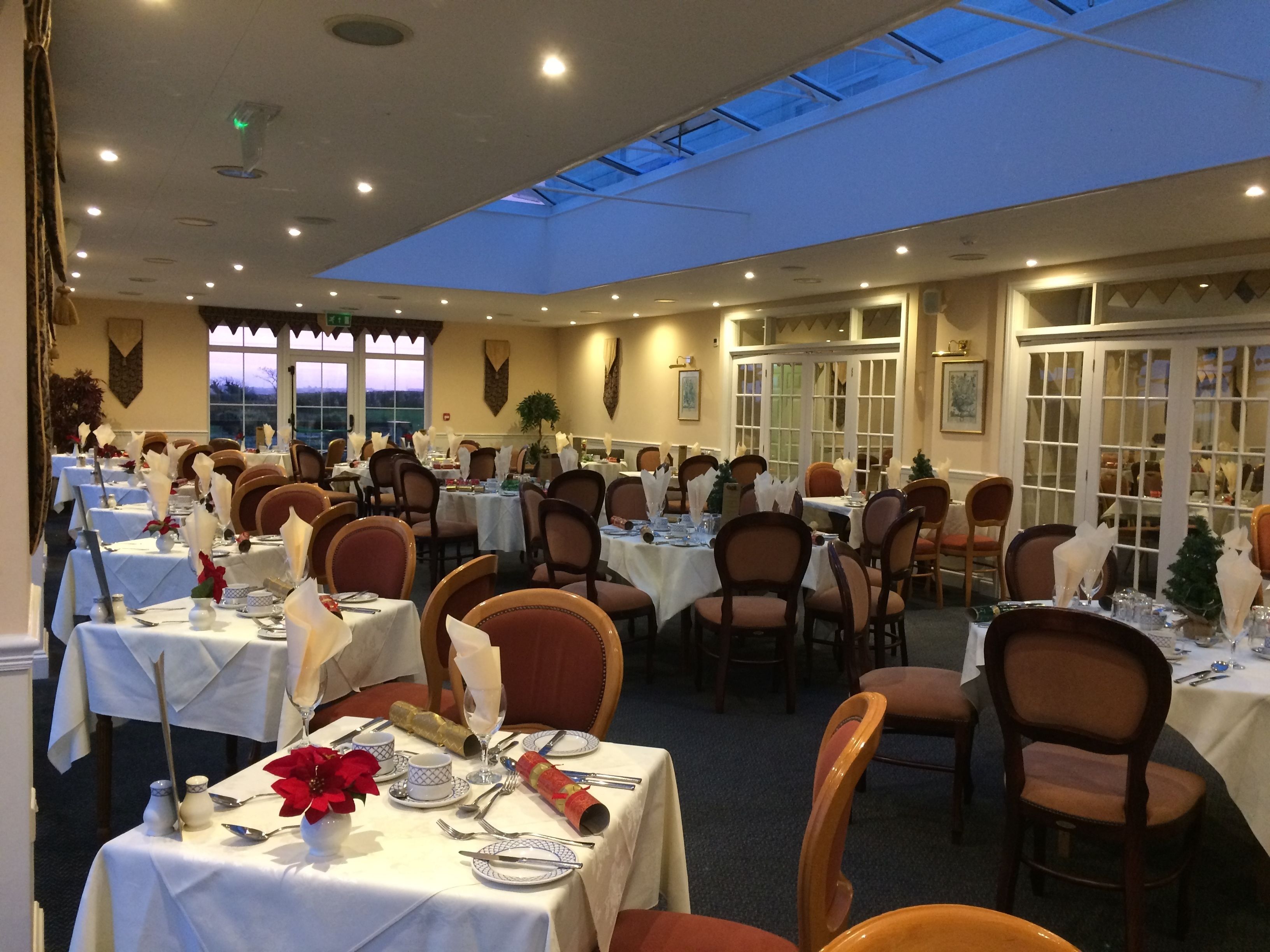 Un salón de banquetes con varias mesas dispuestas para comer, con manteles blancos, flores rojas y cubertería ordenada.