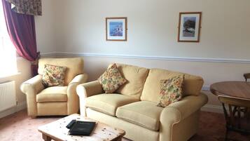 A living room with a beige sofa, two armchairs, a coffee table, and two framed pictures on the wall.
