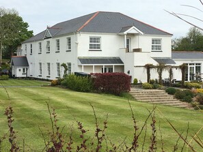 A large, white building with a grey roof, surrounded by a well-maintained lawn and a few bushes. - Beggars Reach Hotel (Milford Haven)