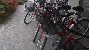 Una hilera de bicicletas rojas estacionadas sobre un camino de ladrillos frente a un edificio con una puerta blanca y un hidrante rojo cercano.