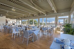 Un comedor amplio con varias mesas y sillas, ventanas grandes que ofrecen vistas al exterior, y un diseño de techo moderno.