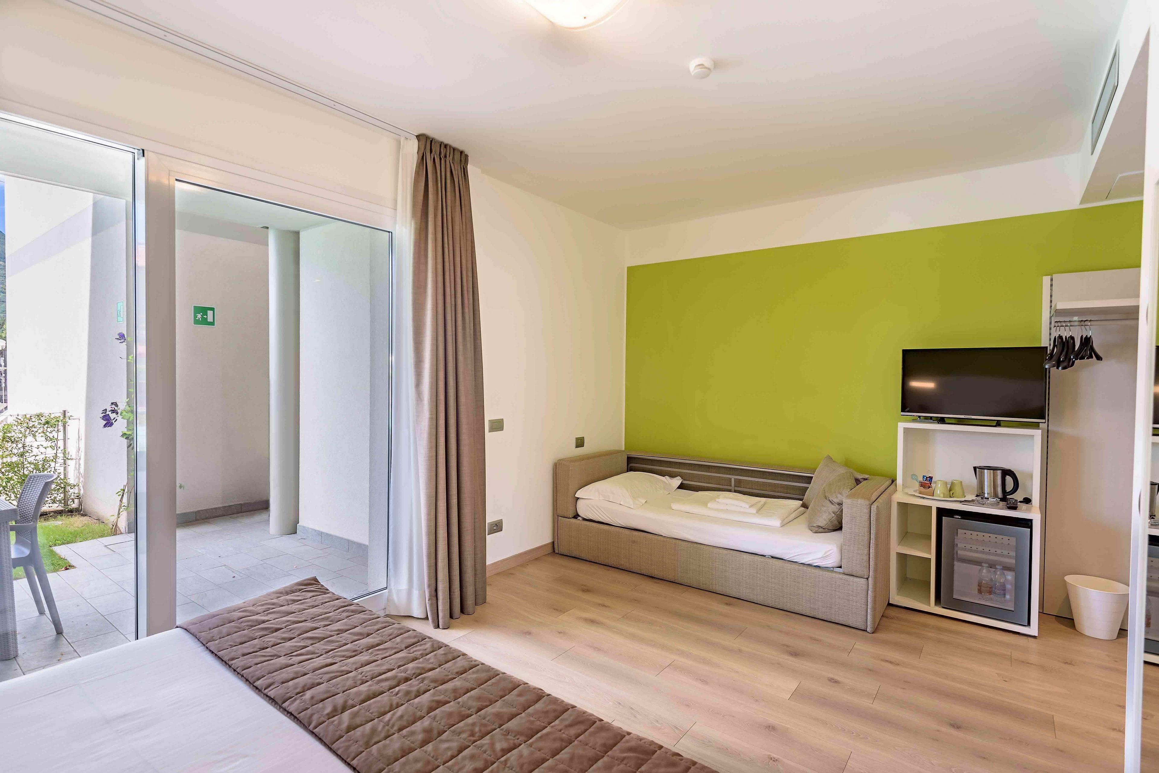 A modern hotel room with a bed, a sofa, a television, and a mini-fridge.