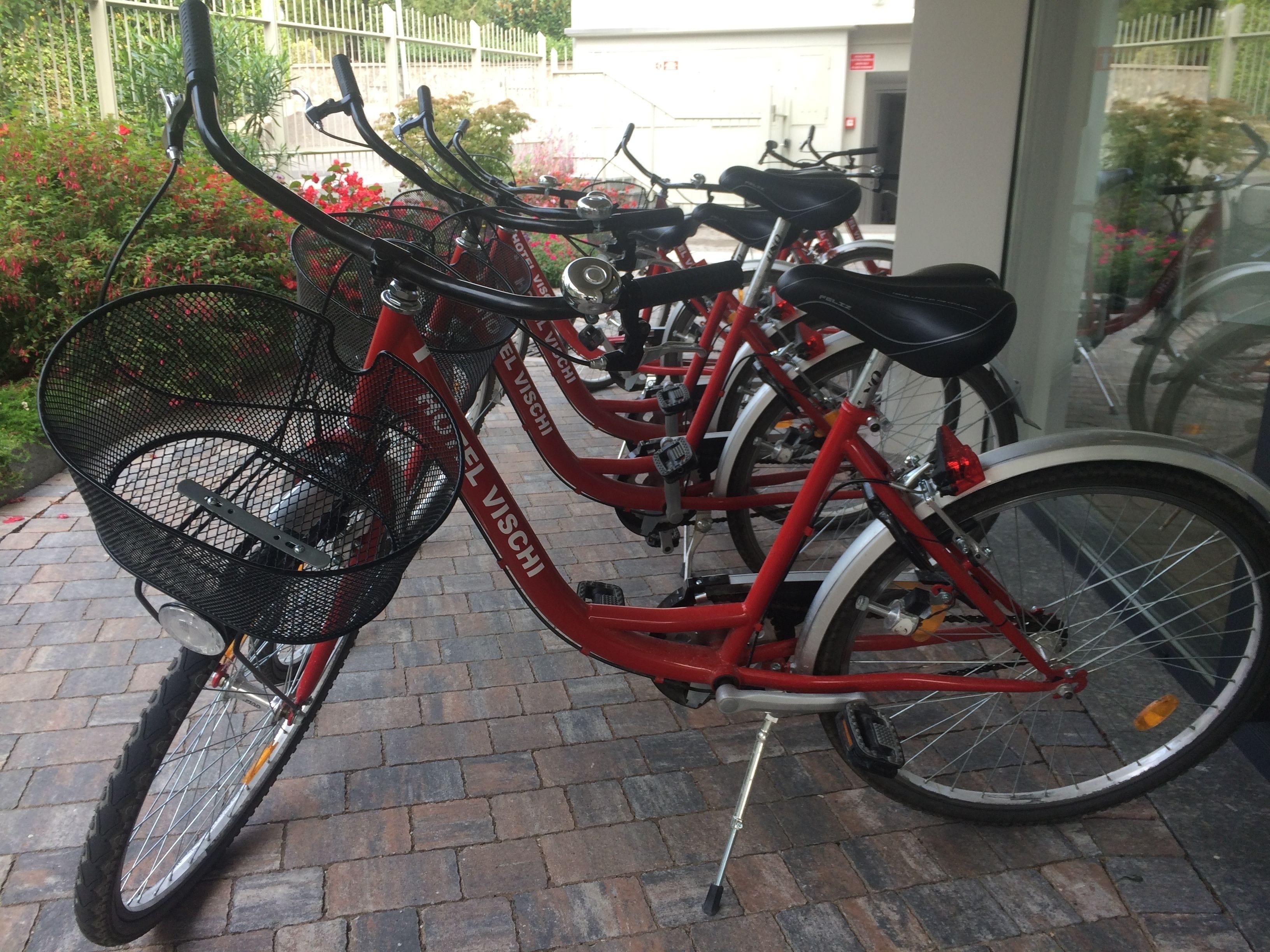 A red bicycle with a basket and a chain guard, parked on a brick pavement.