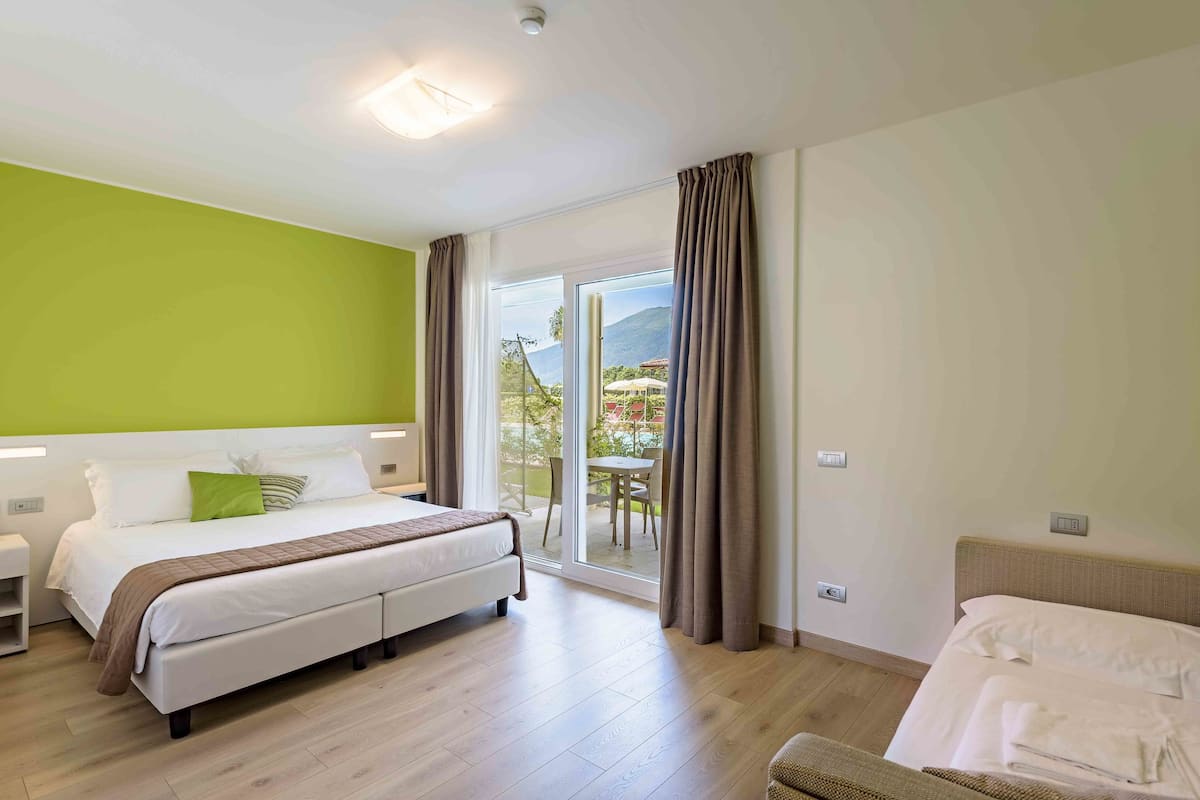 Une chambre d’hôtel comprenant un lit, une chaise, une petite table et une porte-fenêtre coulissante donnant sur un espace extérieur.