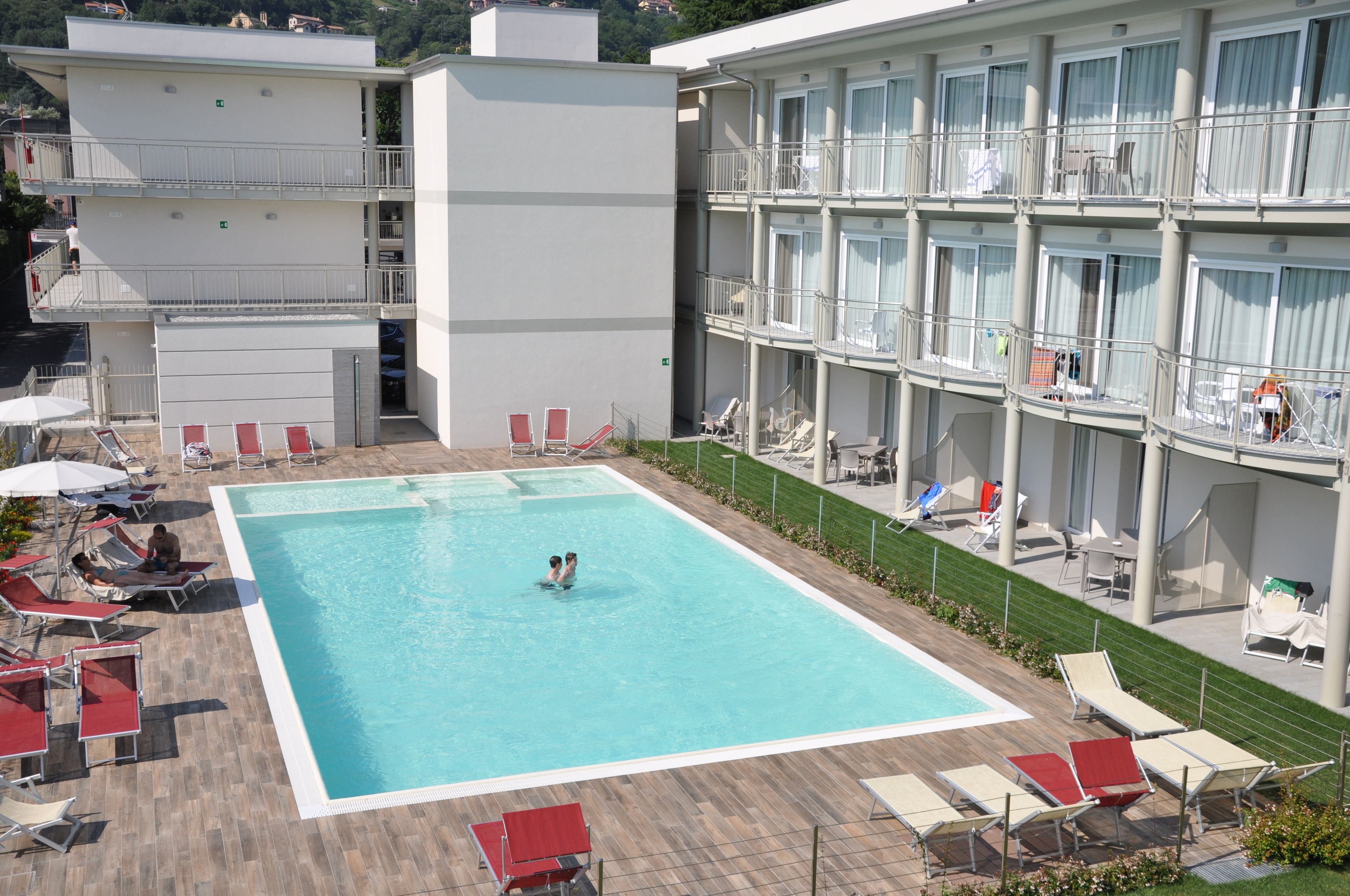 A hotel with a swimming pool surrounded by sun loungers and a covered area.