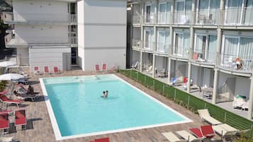 A hotel with a swimming pool surrounded by sun loungers and a covered area.