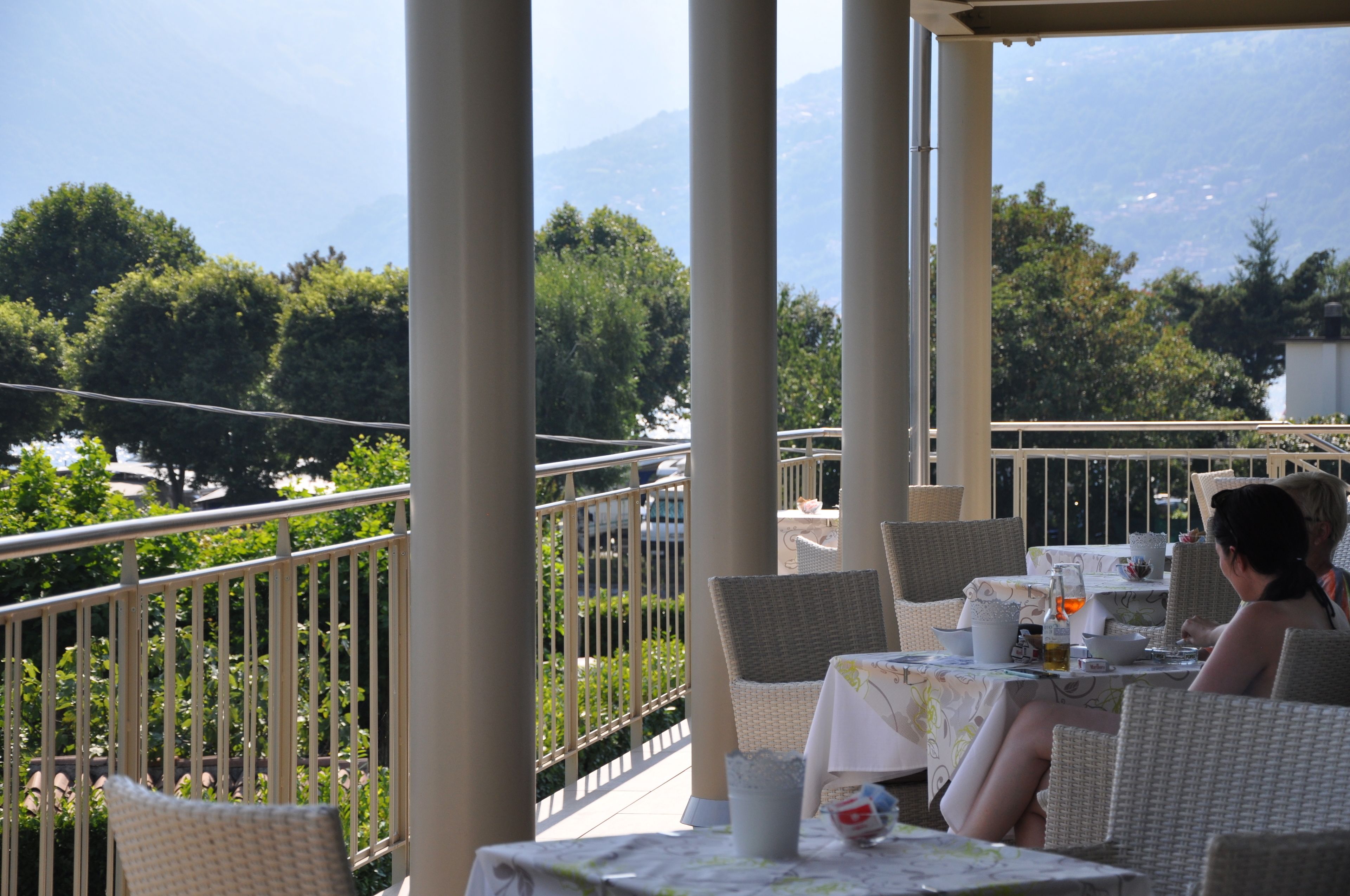 A terrace with wicker chairs and tables, overlooking a mountainous landscape.