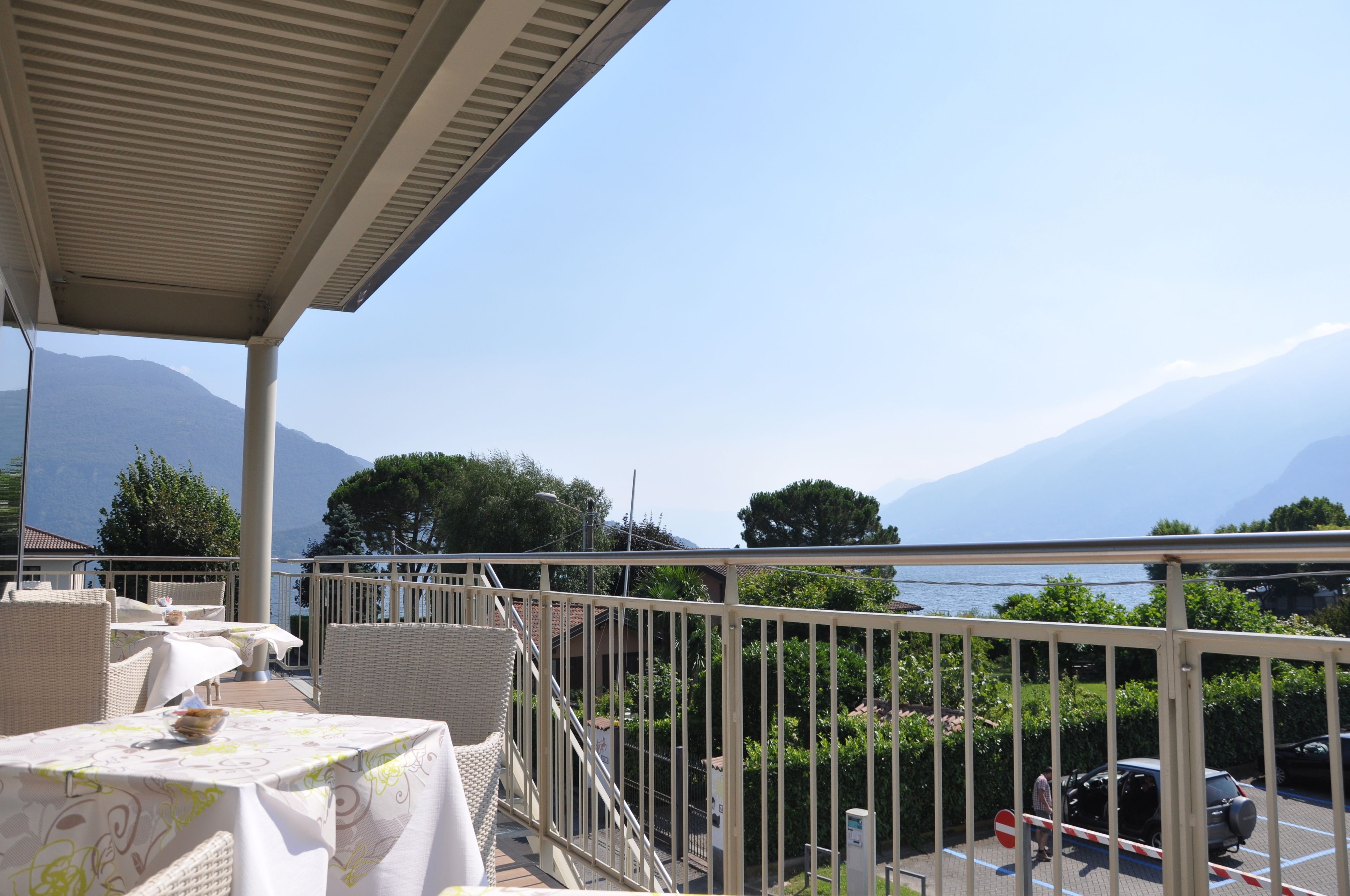 Une terrasse avec des tables et des chaises, offrant une vue sur un plan d’eau et des montagnes.