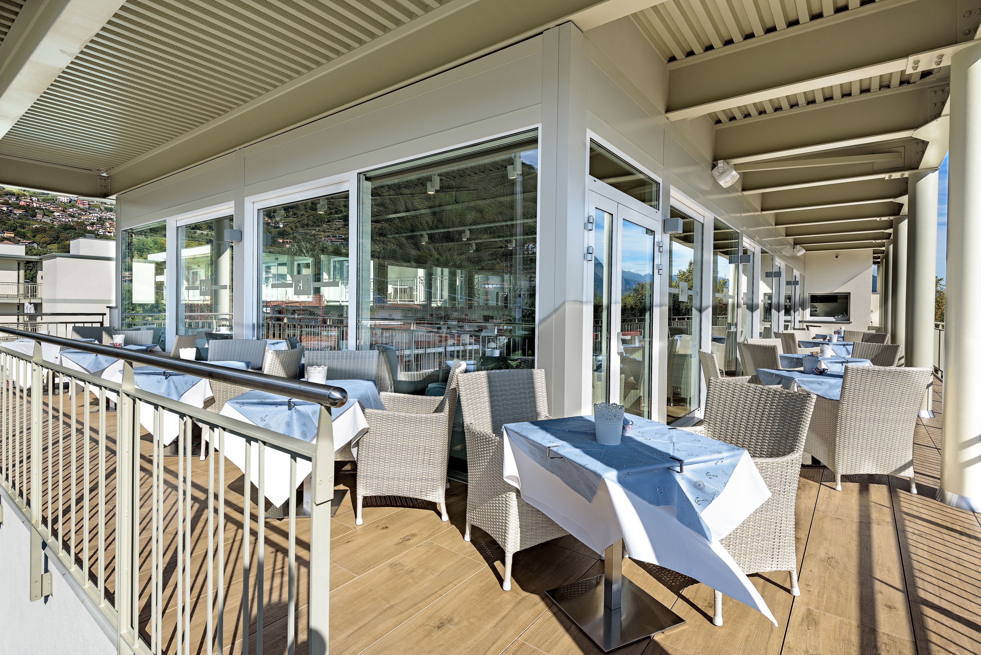 An outdoor dining area with wicker chairs and tables, large windows, and a wooden deck.