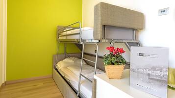 A bunk bed room with a green wall, a wooden headboard, a small table with a potted plant, and a welcome sign.