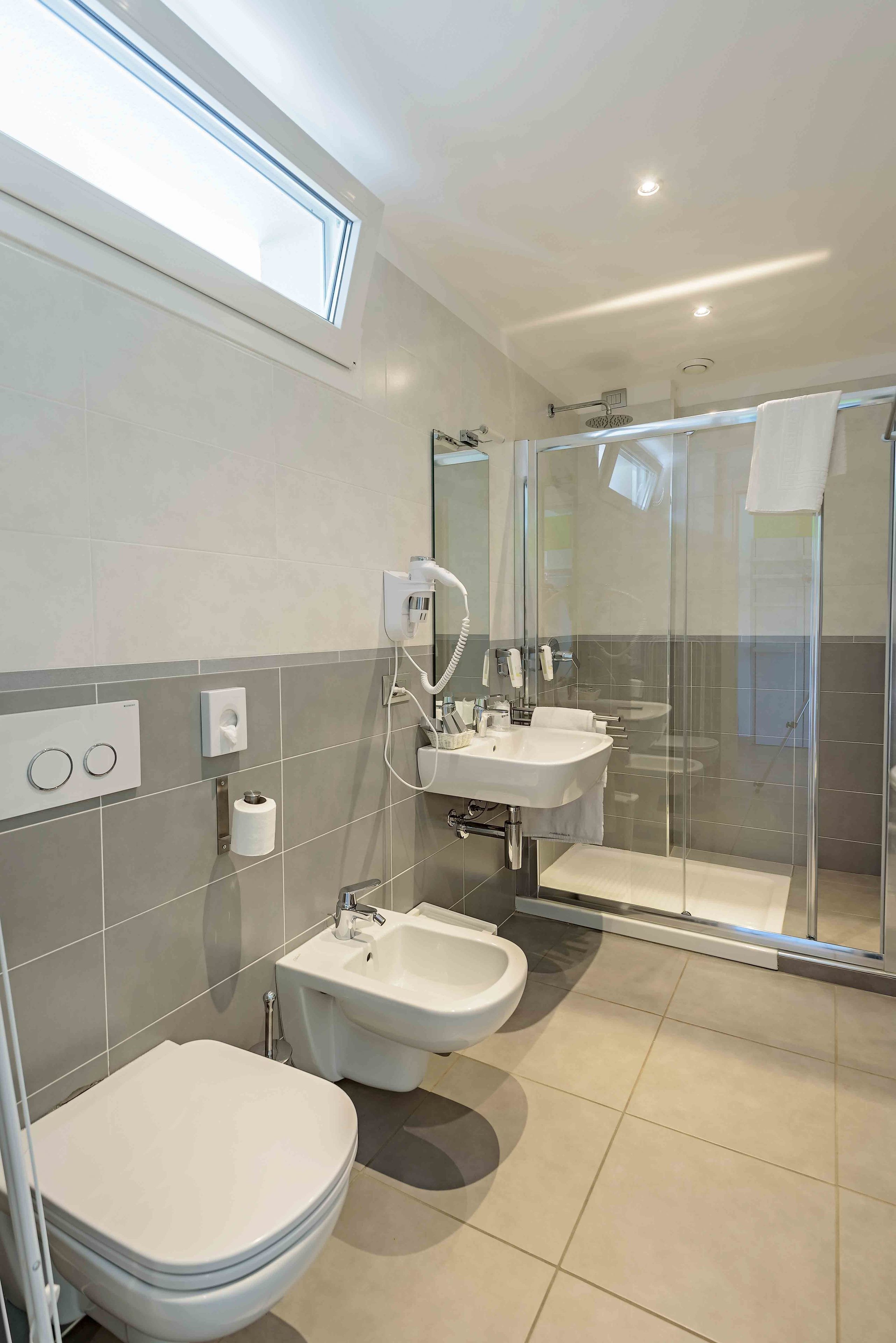 A modern bathroom with a toilet, bidet, two sinks, and a glass-enclosed shower.