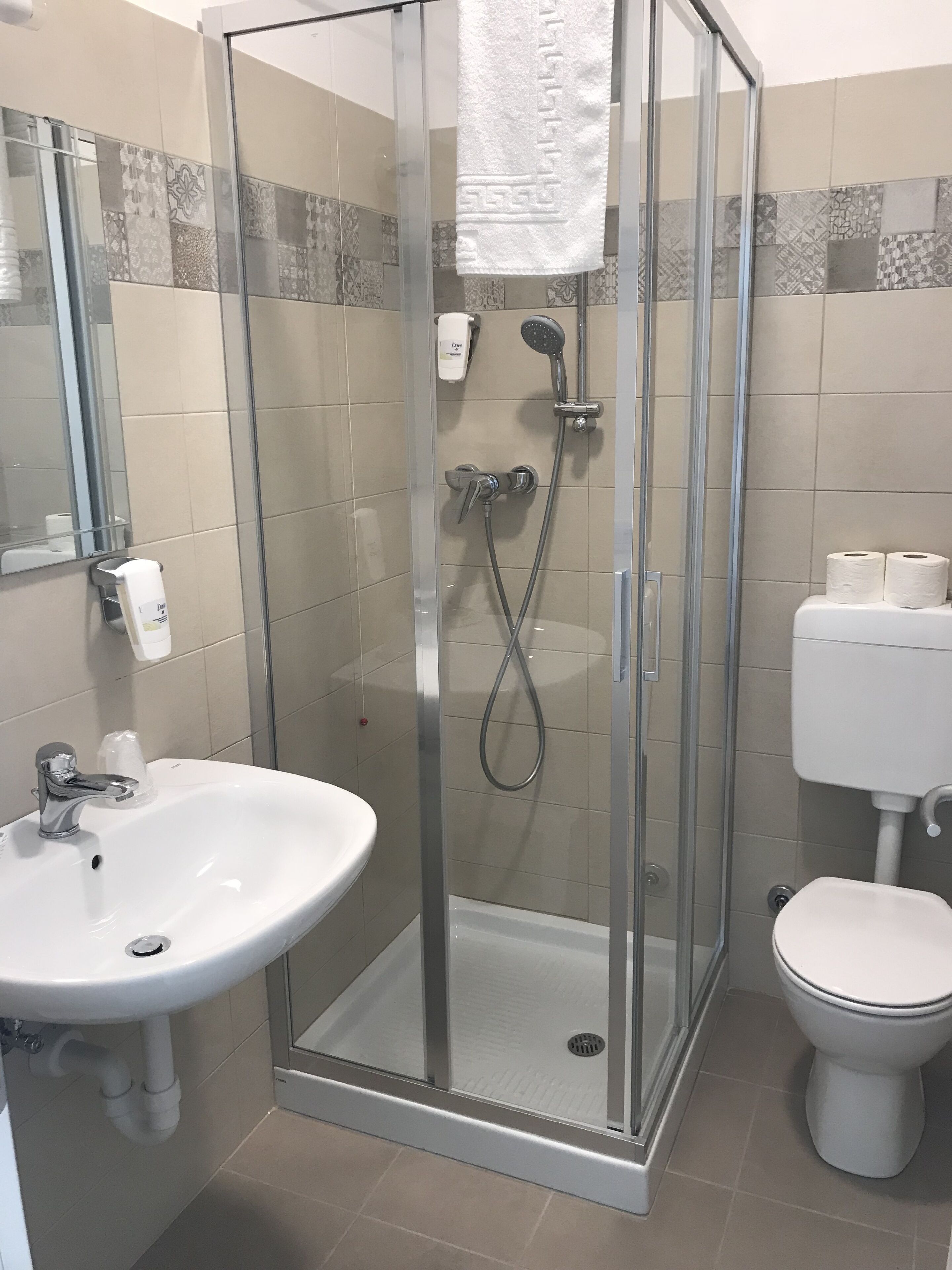 Un baño moderno con ducha de vidrio, lavamanos blanco y retrete.