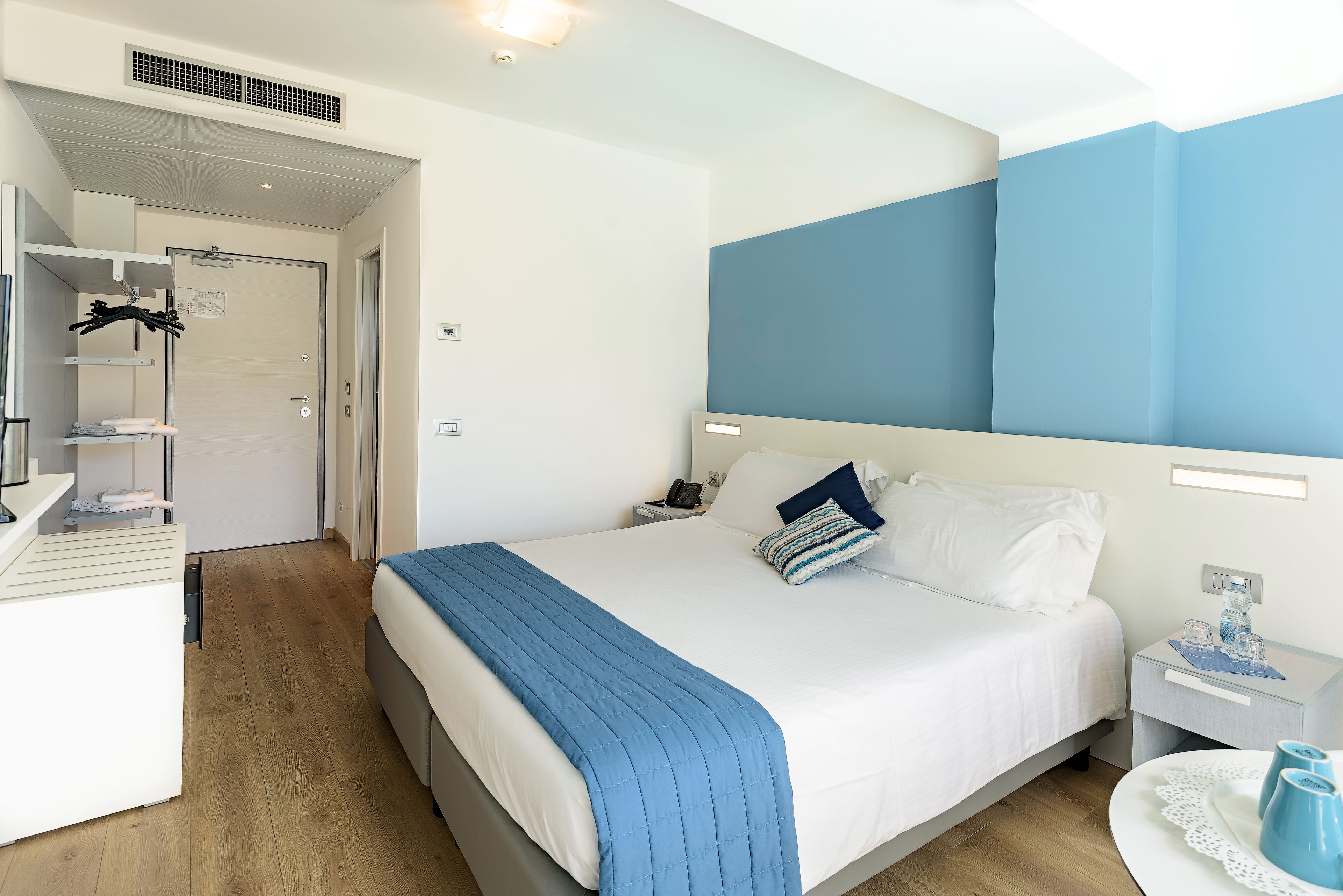 A hotel room with a bed, bedside tables, a desk, and a wardrobe.