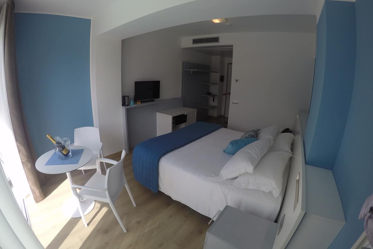 Une chambre d’hôtel avec un lit, un bureau, une chaise, une télévision et une petite table sur laquelle se trouvent une bouteille et un verre.